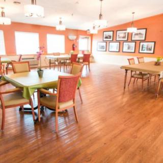 A bright and spacious dining room with wooden floors, colorful chairs, and tables under modern lighting fixtures.