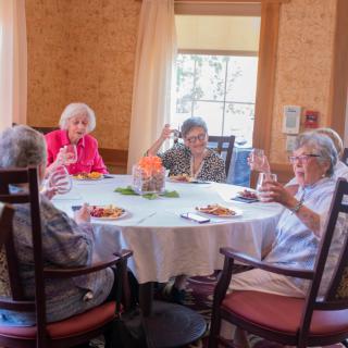 A group of elderly women enjoying a meal and conversation around a dining table.