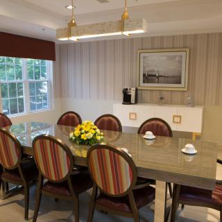 A well-decorated dining room featuring a long table with striped chairs, a centerpiece of yellow flowers, and ambient lighting.