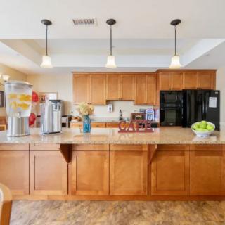 A modern kitchen with wood cabinets, featuring a coffee station and pendant lighting.