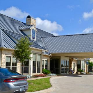 A residential building with a metal roof and a driveway, featuring a parked car.