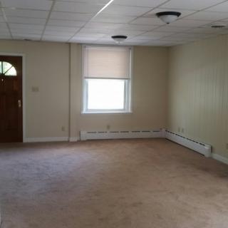 An empty room with carpet flooring, a window, and a wooden door.