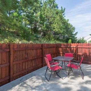 A cozy outdoor patio area with a table and red chairs, surrounded by a wooden fence and lush greenery.