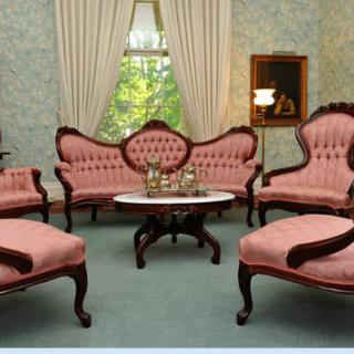 A vintage living room with Victorian-style furniture, including a sofa and armchairs surrounding a coffee table.