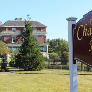 A large brick building with a prominent sign in front, surrounded by trees and grass.