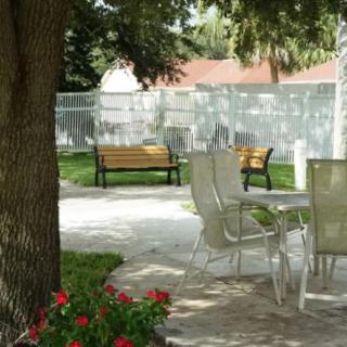 A serene garden setting with outdoor chairs and benches surrounded by trees and flowers.