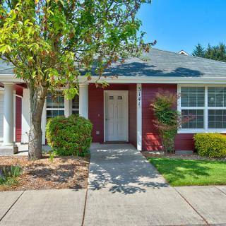 A charming single-story red house with a tidy front yard and a clear sidewalk.