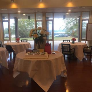 An elegantly decorated dining area prepared for an event, featuring round tables with white tablecloths and floral centerpieces.