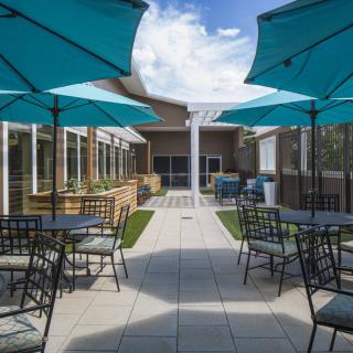 A modern outdoor patio area with blue umbrellas and neatly arranged tables and chairs under a clear sky.