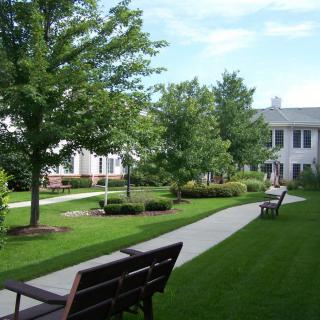 A scenic view of a garden with benches, a pathway, trees, and a building in the background.