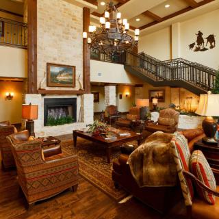 A cozy, rustic living room with a large fireplace, wooden furniture, and a grand chandelier.