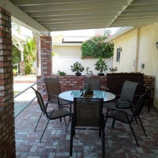 A cozy patio with a glass table surrounded by chairs, framed by brick walls and greenery.