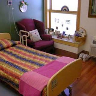 A cozy hospital room featuring a colorful bedspread, an armchair by the window, and various decorative items.