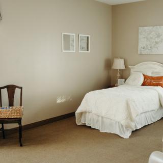 A minimalist bedroom with a single bed, lamp, and chair.
