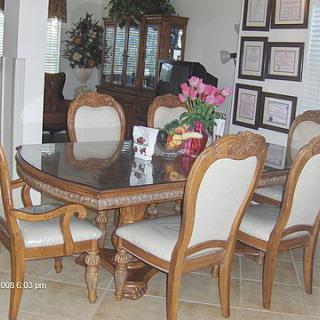 A well-decorated dining room featuring a wooden dining set with a glass top table and upholstered chairs, complemented by a floral arrangement.
