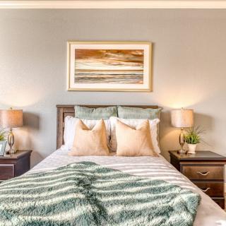 A cozy bedroom featuring a well-decorated bed with pillows, bedside lamps on nightstands, and a framed artwork above the headboard.