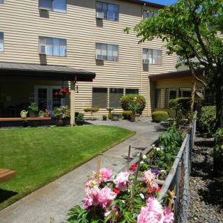 A building with a garden area featuring flowers, a pathway, and greenery.
