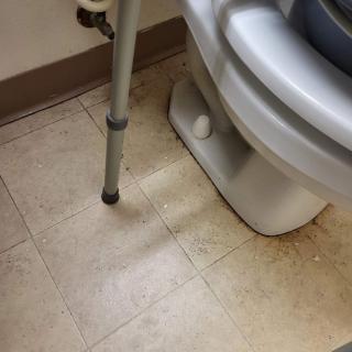 A bathroom with a toilet and grab bar on a tiled floor.