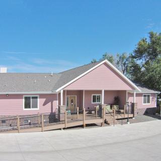 A charming pink house with a porch and surrounding trees on a sunny day.