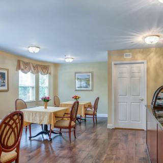 A cozy dining room with tables and chairs, featuring hardwood floors and soft lighting.