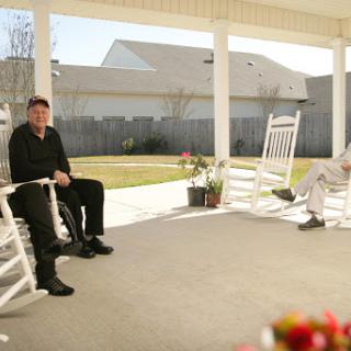 Two individuals enjoying a sunny day on the porch, seated in rocking chairs.