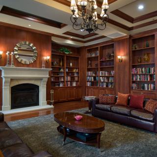 A luxurious library living room with leather sofas, built-in bookshelves, and a fireplace.