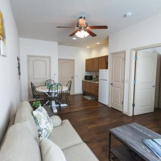 A cozy living area with a connected kitchen and dining space featuring a beige sofa, wooden furniture, and ceiling fan.