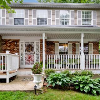 A charming colonial-style house with a brick facade and inviting front porch, surrounded by lush greenery.
