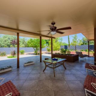 A spacious covered patio area with comfortable seating and a ceiling fan, overlooking a well-maintained garden.