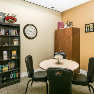 A small office meeting room with a round table, chairs, and a bookshelf.