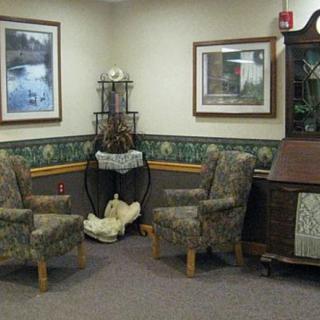 A cozy living room corner with two patterned chairs, artwork on the walls, and a vintage cabinet.