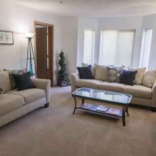 A cozy living room featuring two beige sofas, a glass coffee table, and a floor lamp.
