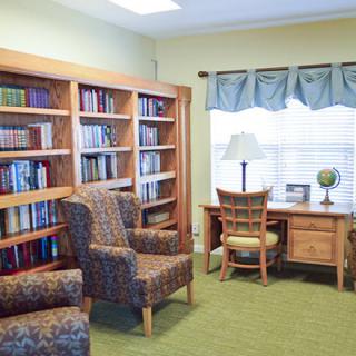 A cozy library corner with bookshelves, chairs, and a desk by the window.