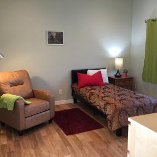 A cozy bedroom with a single bed, armchair, and nightstand.