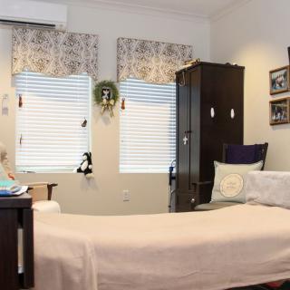 A cozy bedroom with a neatly made bed, wooden furniture, and decorated windows.