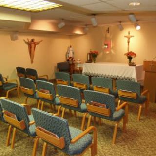 A small chapel with rows of chairs facing an altar, adorned with a cross and crucifix.