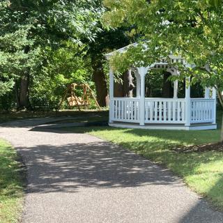 A peaceful outdoor scene featuring a white gazebo surrounded by trees along a winding pathway.