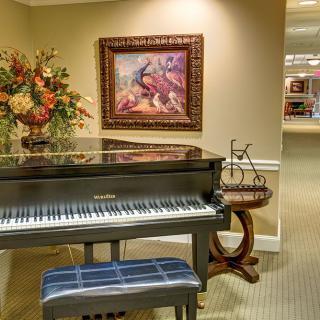 A stylish interior featuring a grand piano with a bench, adorned with artwork and floral arrangements.
