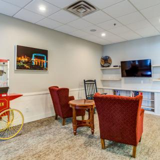 A cozy lounge area with red chairs, a table, a television mounted on the wall, and a popcorn machine.