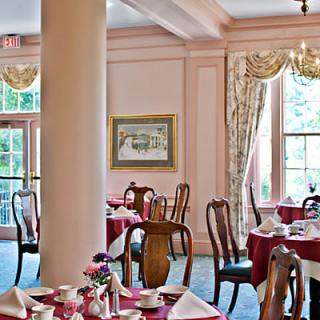 An elegant restaurant dining room with neatly arranged tables, adorned with classic decor and large windows.