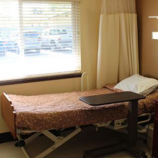 A hospital room with a single bed and a tray table near the window.