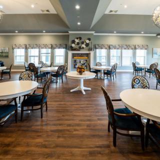 A spacious dining area with round tables and chairs, featuring a fireplace and large windows.