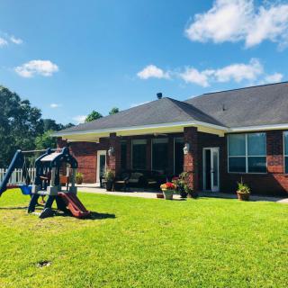A sunny backyard featuring a swing set, vibrant green grass, and a cozy patio area.