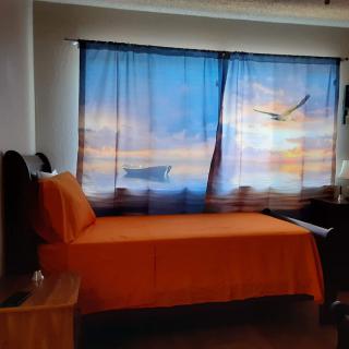 A cozy bedroom with orange bedding and scenic curtains depicting a sunset and bird.