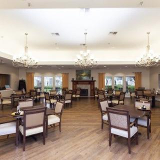 An elegant dining room with multiple tables and chairs, featuring chandeliers and a hardwood floor.