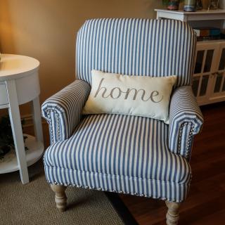 A cozy striped armchair with a decorative 'home' cushion in a warmly lit living room.