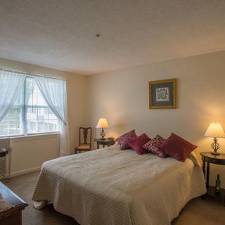 A cozy bedroom with a neatly made bed, warm lighting from two lamps, and a window allowing natural light to filter in.