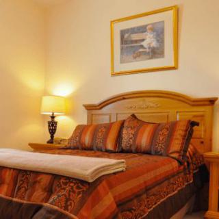 A cozy bedroom with a well-made bed, bedside lamp, and framed artwork on the wall.