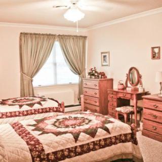 A cozy bedroom featuring two twin beds with quilt covers, vintage wooden furniture including a dresser and vanity table, complemented by elegant curtains.