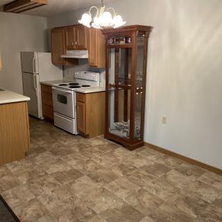 A spacious kitchen with wooden cabinets, a stove, and refrigerator, featuring tile flooring and a china cabinet.